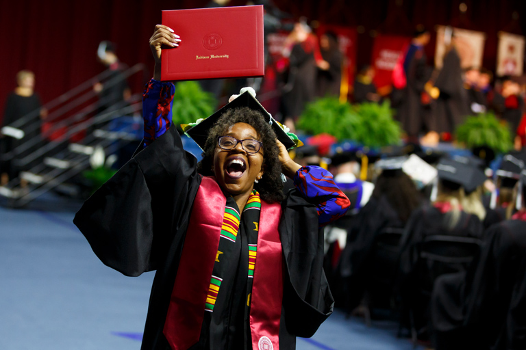 A woman coming off the Commencement stage exults with her new diploma