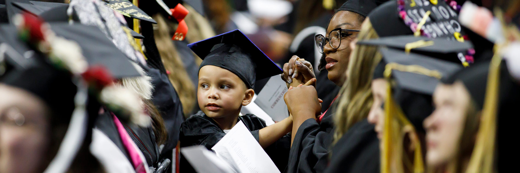 A little boy wearing his own grad cap sits on his mother's lap during her IU South Bend graduation ceremony.