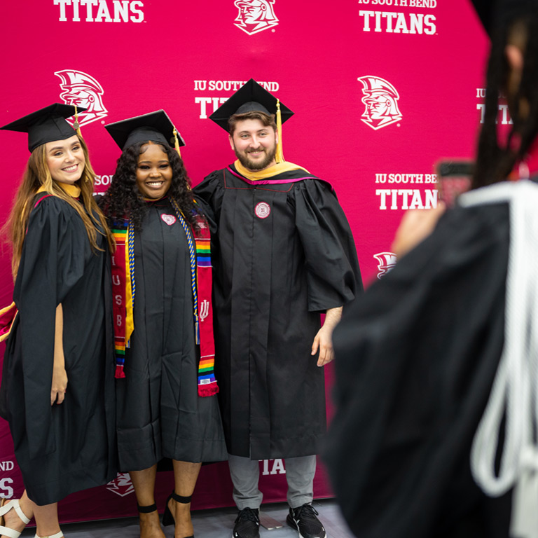 Two young women and a man post for post-Commencement pictures in front of a Titans backdrop